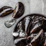 Fresh uncooked big mussels on ice. Slate background.